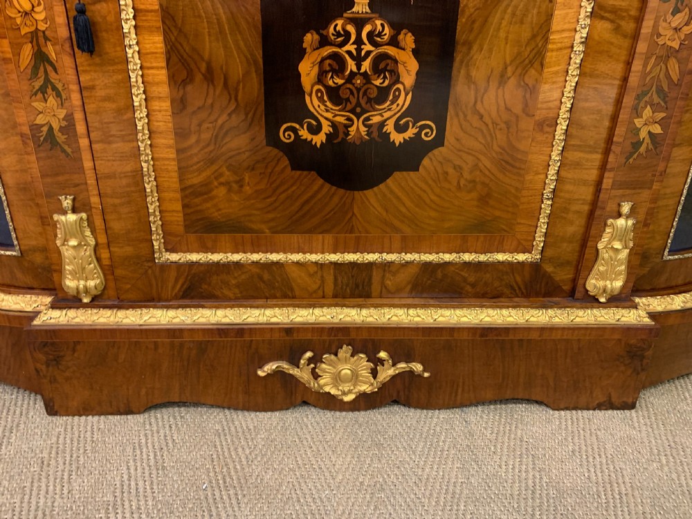 A Victorian burr walnut credenza featuring floral marquetry inlays, gilt bronze ormolu mounts, a central panelled door, and curved glazed side cabinets. View XI