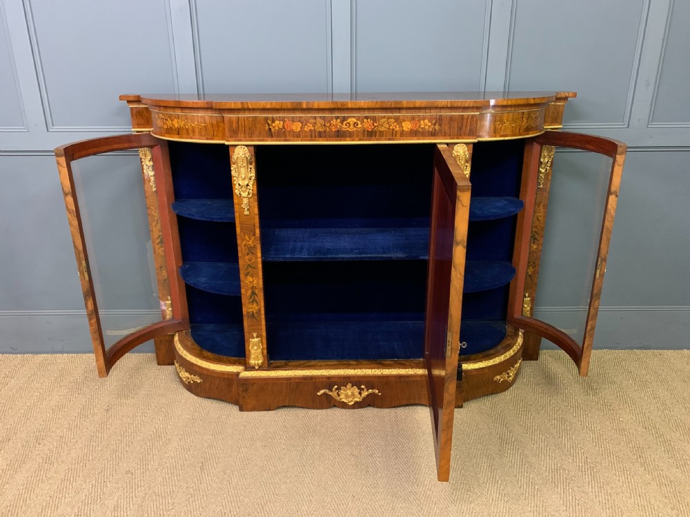 A Victorian burr walnut credenza featuring floral marquetry inlays, gilt bronze ormolu mounts, a central panelled door, and curved glazed side cabinets. View XII