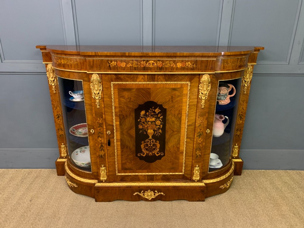 A Victorian burr walnut credenza featuring floral marquetry inlays, gilt bronze ormolu mounts, a central panelled door, and curved glazed side cabinets. View XIII
