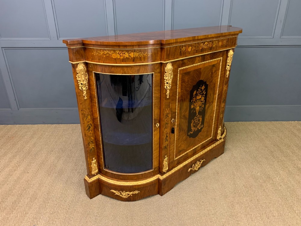 A Victorian burr walnut credenza featuring floral marquetry inlays, gilt bronze ormolu mounts, a central panelled door, and curved glazed side cabinets. View XV