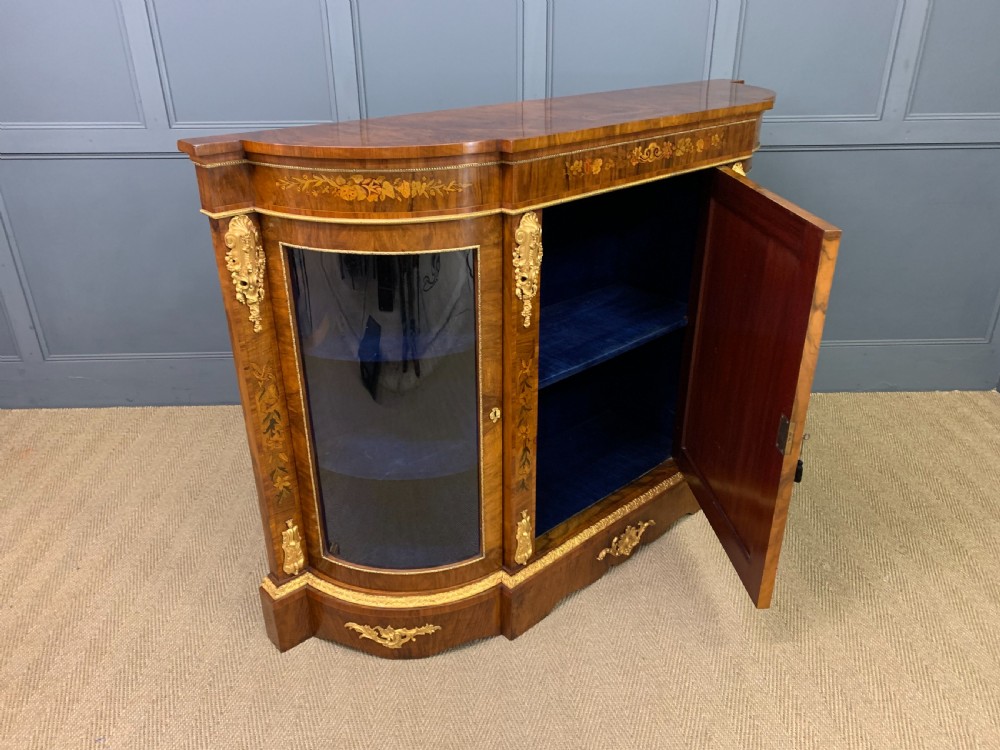 A Victorian burr walnut credenza featuring floral marquetry inlays, gilt bronze ormolu mounts, a central panelled door, and curved glazed side cabinets. View XVI