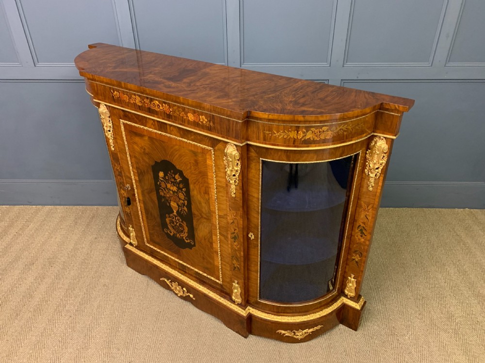A Victorian burr walnut credenza featuring floral marquetry inlays, gilt bronze ormolu mounts, a central panelled door, and curved glazed side cabinets. View XVII