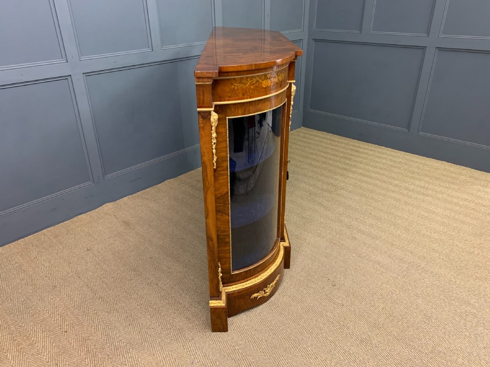 A Victorian burr walnut credenza featuring floral marquetry inlays, gilt bronze ormolu mounts, a central panelled door, and curved glazed side cabinets. View XVIII
