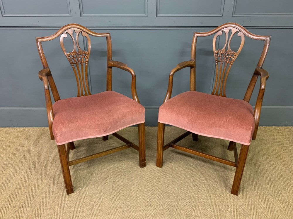 A pair of Georgian mahogany open armchairs with carved pierced splat backs and rose-coloured upholstered seats.