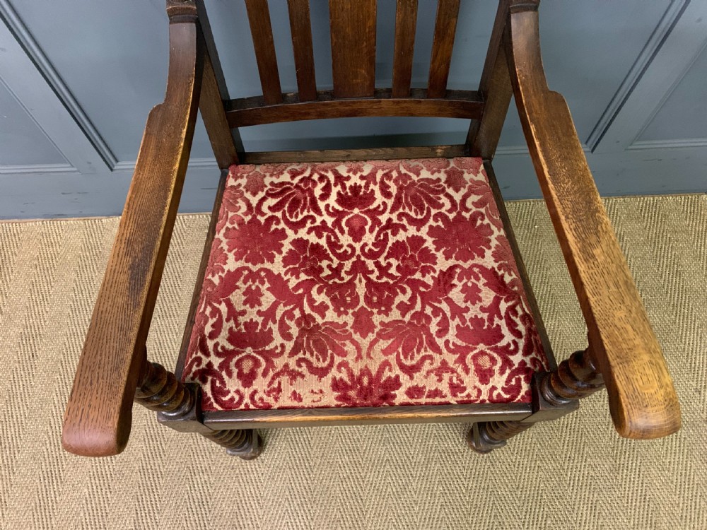 A dark oak armchair with barley twist uprights, a carved cresting rail, a vertical slat back, and a red patterned velvet upholstered seat pad. View III