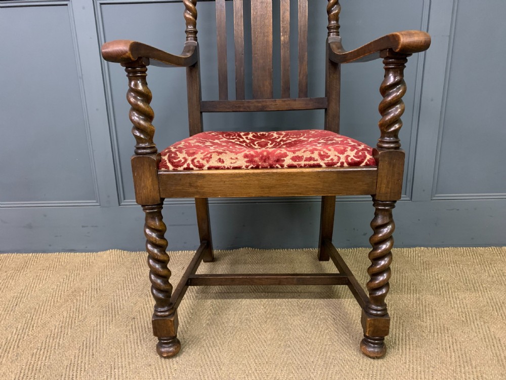A dark oak armchair with barley twist uprights, a carved cresting rail, a vertical slat back, and a red patterned velvet upholstered seat pad. View IV