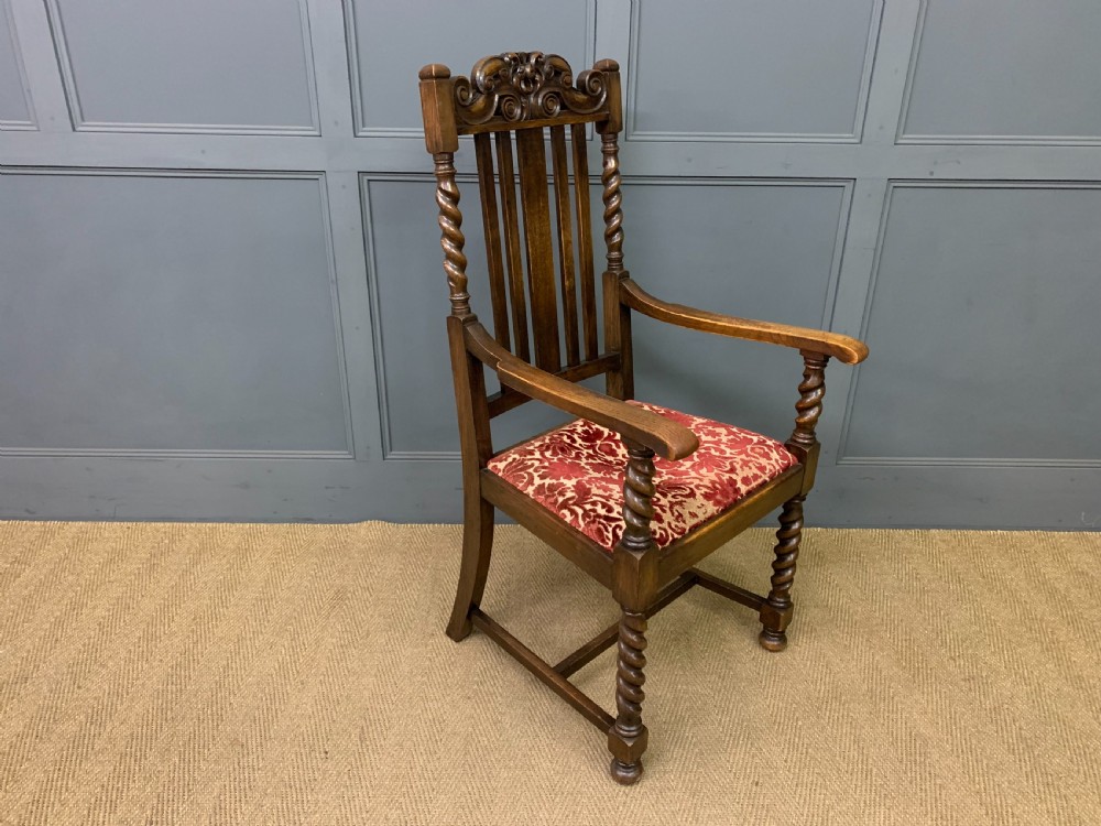A dark oak armchair with barley twist uprights, a carved cresting rail, a vertical slat back, and a red patterned velvet upholstered seat pad. View V