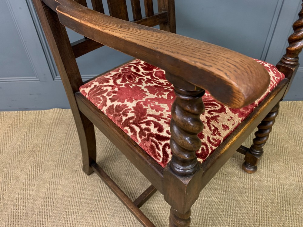 A dark oak armchair with barley twist uprights, a carved cresting rail, a vertical slat back, and a red patterned velvet upholstered seat pad. View VI