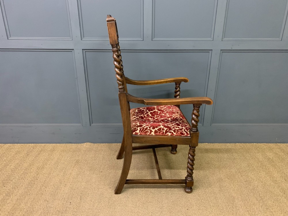 A dark oak armchair with barley twist uprights, a carved cresting rail, a vertical slat back, and a red patterned velvet upholstered seat pad. View VII