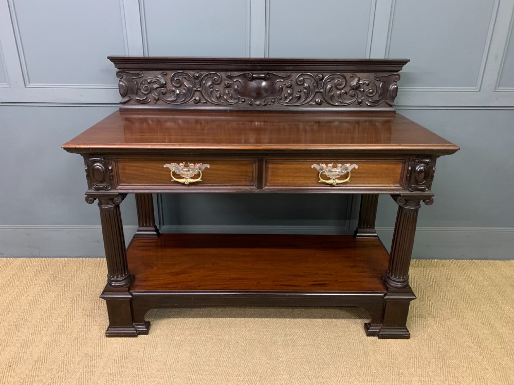 A Victorian mahogany buffet featuring a carved scroll backboard, two frieze drawers with brass handles, fluted support columns, and an open lower tier. View II