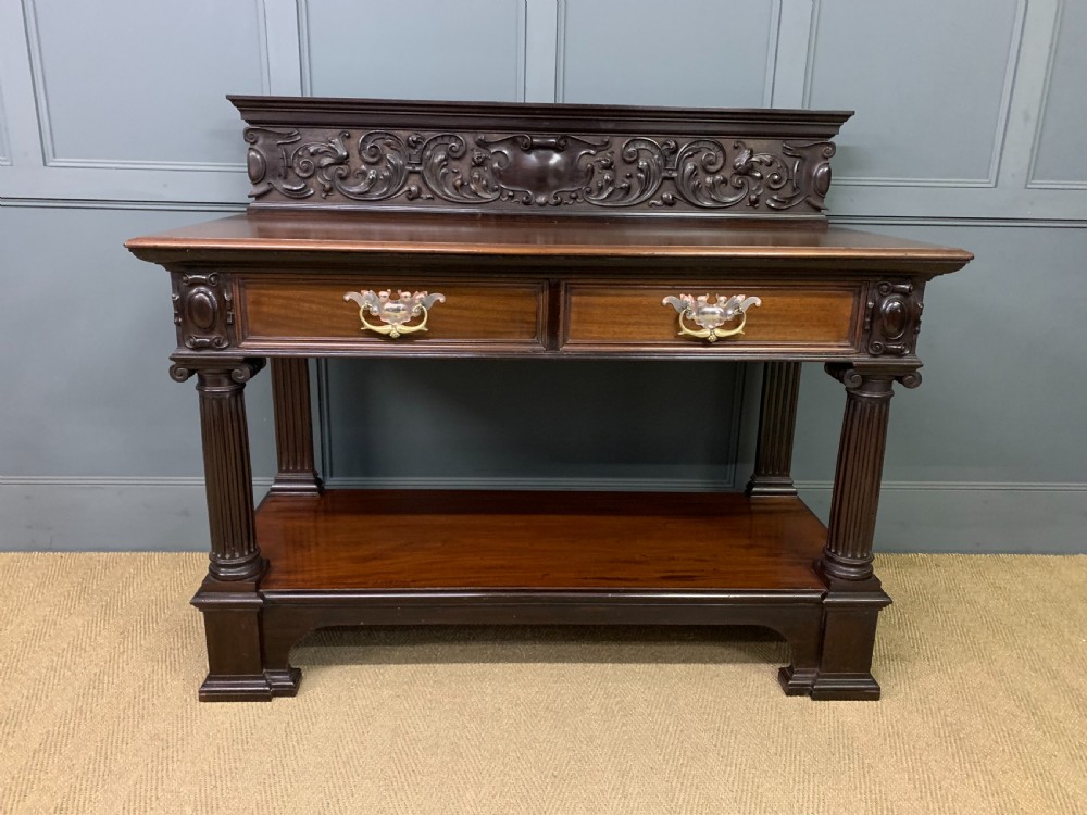 A Victorian mahogany buffet featuring a carved scroll backboard, two frieze drawers with brass handles, fluted support columns, and an open lower tier. View III