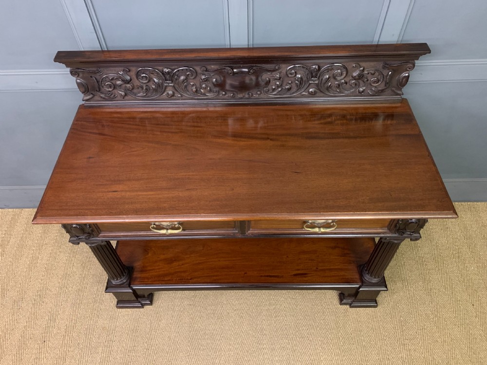 A Victorian mahogany buffet featuring a carved scroll backboard, two frieze drawers with brass handles, fluted support columns, and an open lower tier. View IV