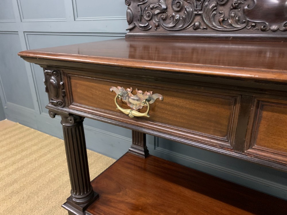 A Victorian mahogany buffet featuring a carved scroll backboard, two frieze drawers with brass handles, fluted support columns, and an open lower tier. View V