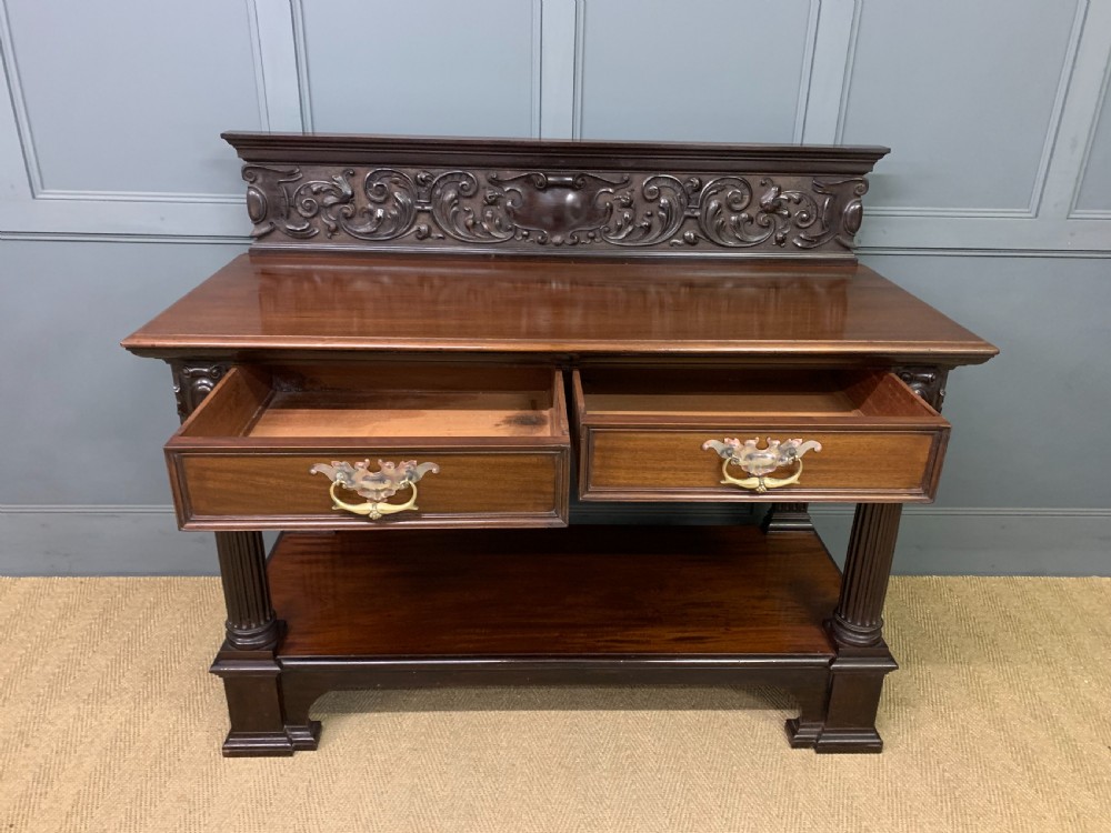 A Victorian mahogany buffet featuring a carved scroll backboard, two frieze drawers with brass handles, fluted support columns, and an open lower tier. View XI