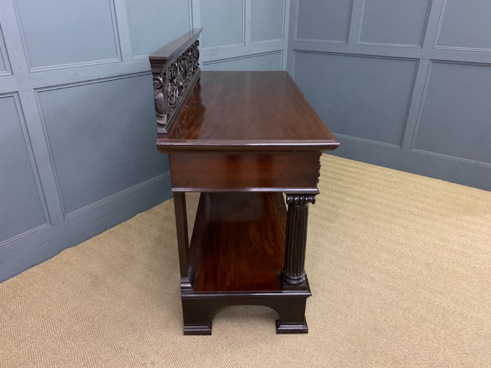 A Victorian mahogany buffet featuring a carved scroll backboard, two frieze drawers with brass handles, fluted support columns, and an open lower tier. View XII