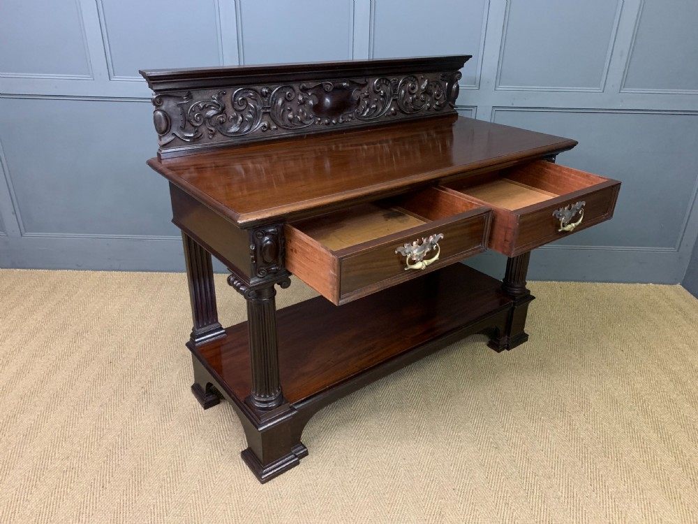 A Victorian mahogany buffet featuring a carved scroll backboard, two frieze drawers with brass handles, fluted support columns, and an open lower tier. View XIV
