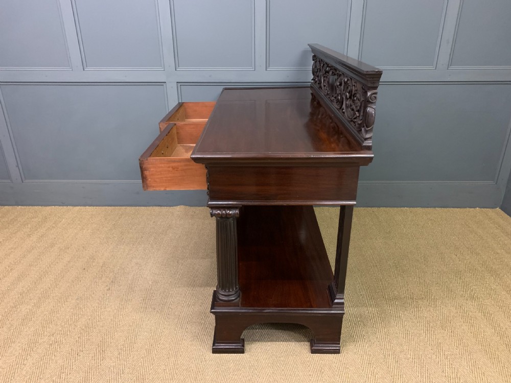 A Victorian mahogany buffet featuring a carved scroll backboard, two frieze drawers with brass handles, fluted support columns, and an open lower tier. View XVI
