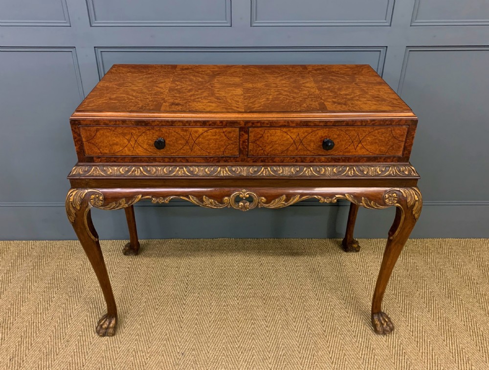 A burr walnut side table featuring two drawers with feather banding, carved egg-and-dart moulding, gilded accents, cabriole legs, and ball-and-claw feet.