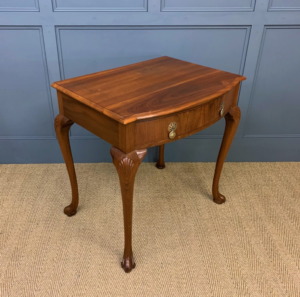 A warm brown burr walnut side table featuring a curved drawer front with brass handles and carved cabriole legs.