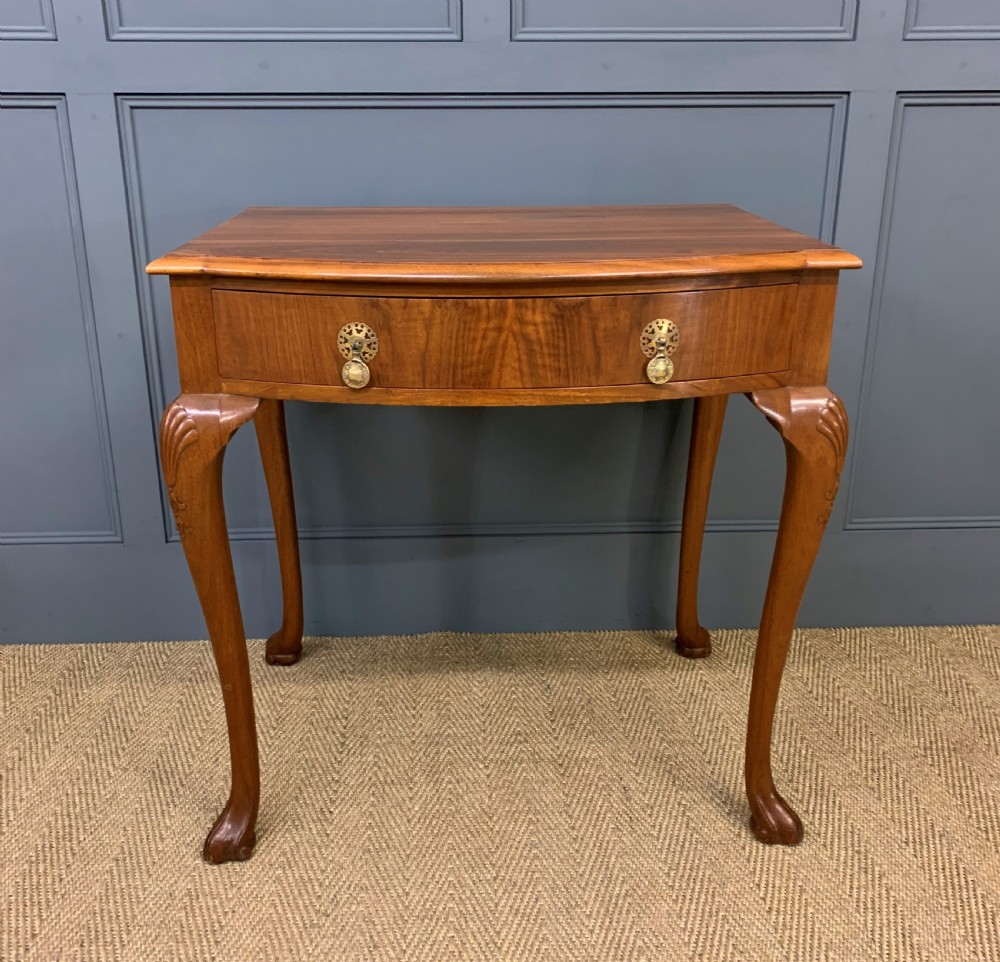 A warm brown burr walnut side table featuring a curved drawer front with brass handles and carved cabriole legs. View IV