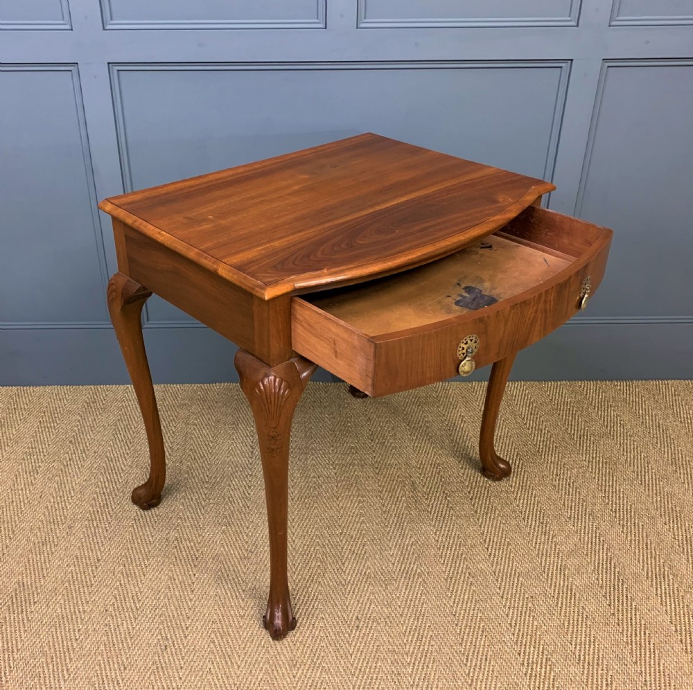 A warm brown burr walnut side table featuring a curved drawer front with brass handles and carved cabriole legs. View VII
