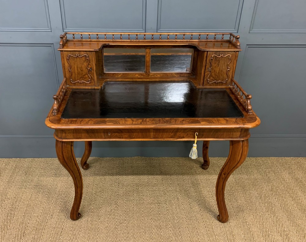 A 19th-century burr walnut bonheur du jour writing desk with a dark leather top, slender cabriole legs, and a gallery section featuring mirrors and small side cabinets.
