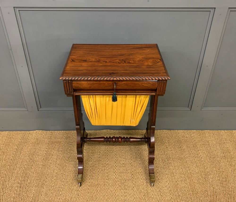 A Regency rosewood work table featuring a rectangular top with carved edging, a single drawer, a pleated yellow fabric storage well below, and trestle legs with brass castors. View II