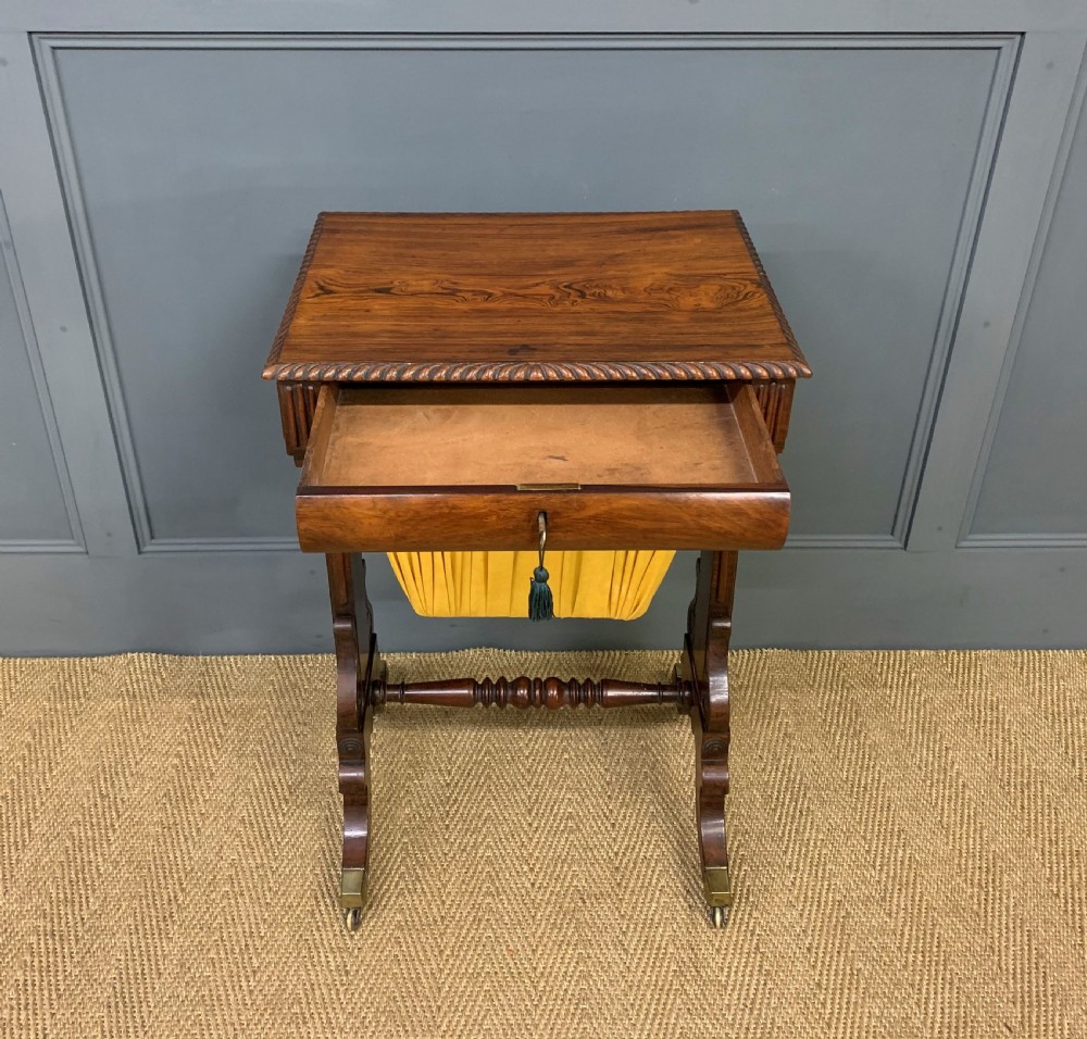A Regency rosewood work table featuring a rectangular top with carved edging, a single drawer, a pleated yellow fabric storage well below, and trestle legs with brass castors. View V