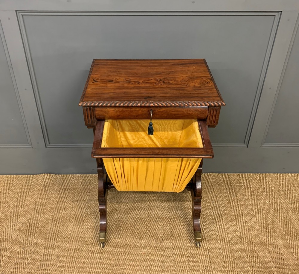 A Regency rosewood work table featuring a rectangular top with carved edging, a single drawer, a pleated yellow fabric storage well below, and trestle legs with brass castors. View VI