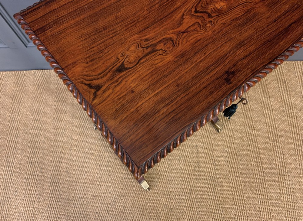 A Regency rosewood work table featuring a rectangular top with carved edging, a single drawer, a pleated yellow fabric storage well below, and trestle legs with brass castors. View VIII