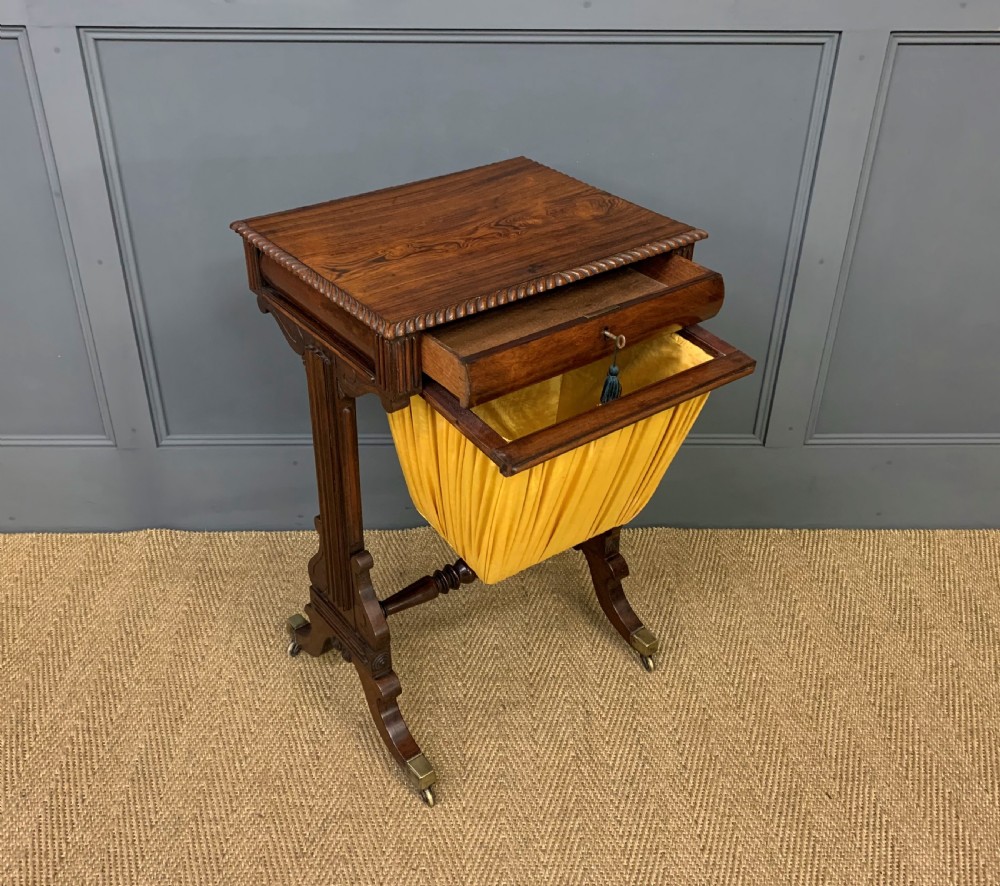 A Regency rosewood work table featuring a rectangular top with carved edging, a single drawer, a pleated yellow fabric storage well below, and trestle legs with brass castors. View IX