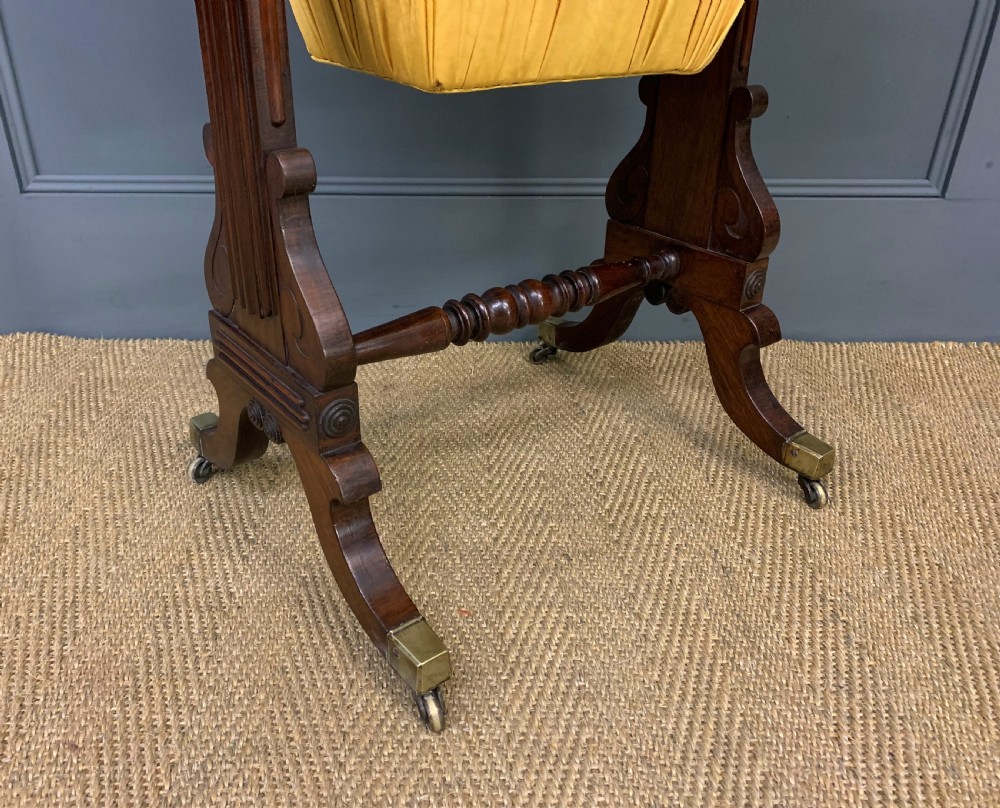 A Regency rosewood work table featuring a rectangular top with carved edging, a single drawer, a pleated yellow fabric storage well below, and trestle legs with brass castors. View X