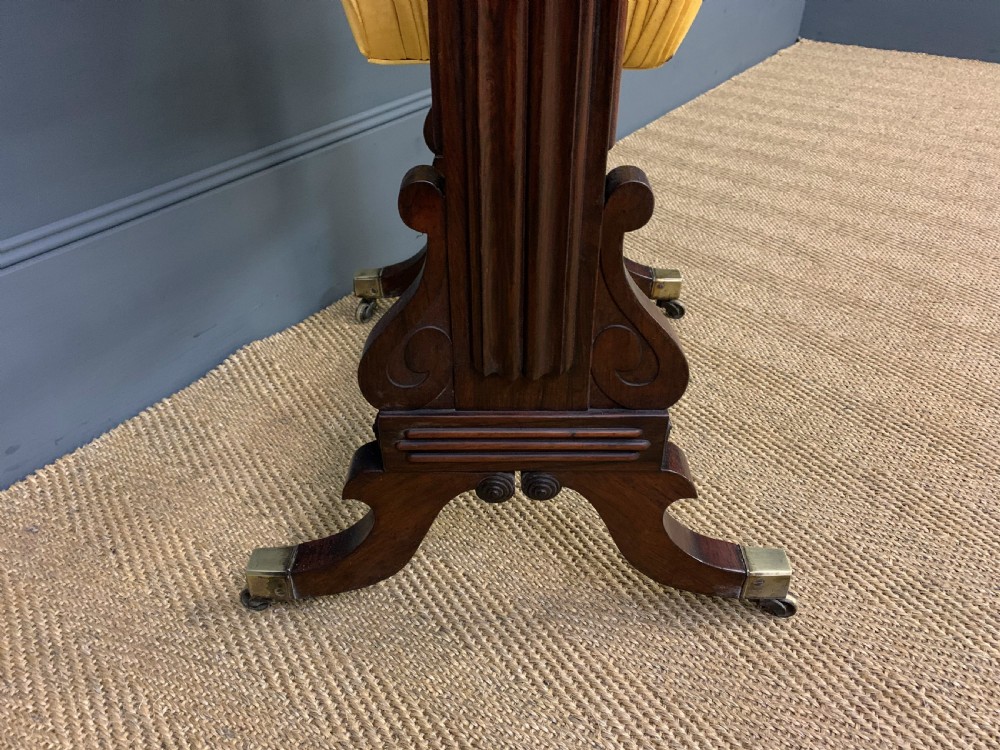 A Regency rosewood work table featuring a rectangular top with carved edging, a single drawer, a pleated yellow fabric storage well below, and trestle legs with brass castors. View XII