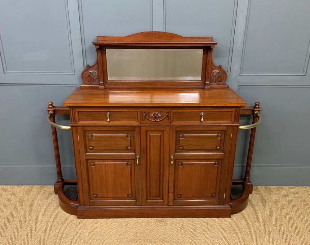 A Victorian walnut hall cupboard featuring a mirror back, two frieze drawers, panelled lower doors, and integrated side umbrella stands with brass rails.