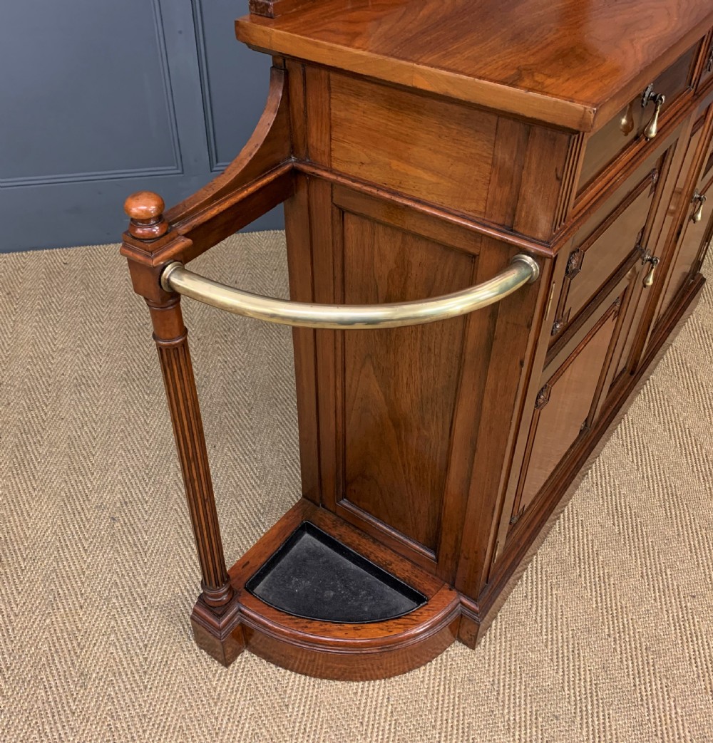 A Victorian walnut hall cupboard featuring a mirror back, two frieze drawers, panelled lower doors, and integrated side umbrella stands with brass rails. View XII