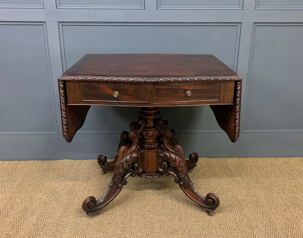 A 19th-century dark rosewood sofa table featuring drop leaves, two front frieze drawers, and an intricately carved central pedestal on scroll legs. View II