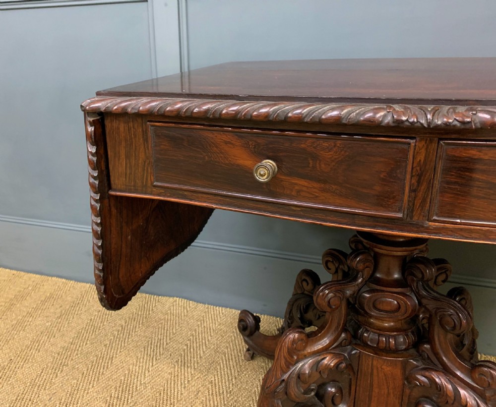 A 19th-century dark rosewood sofa table featuring drop leaves, two front frieze drawers, and an intricately carved central pedestal on scroll legs. View IV