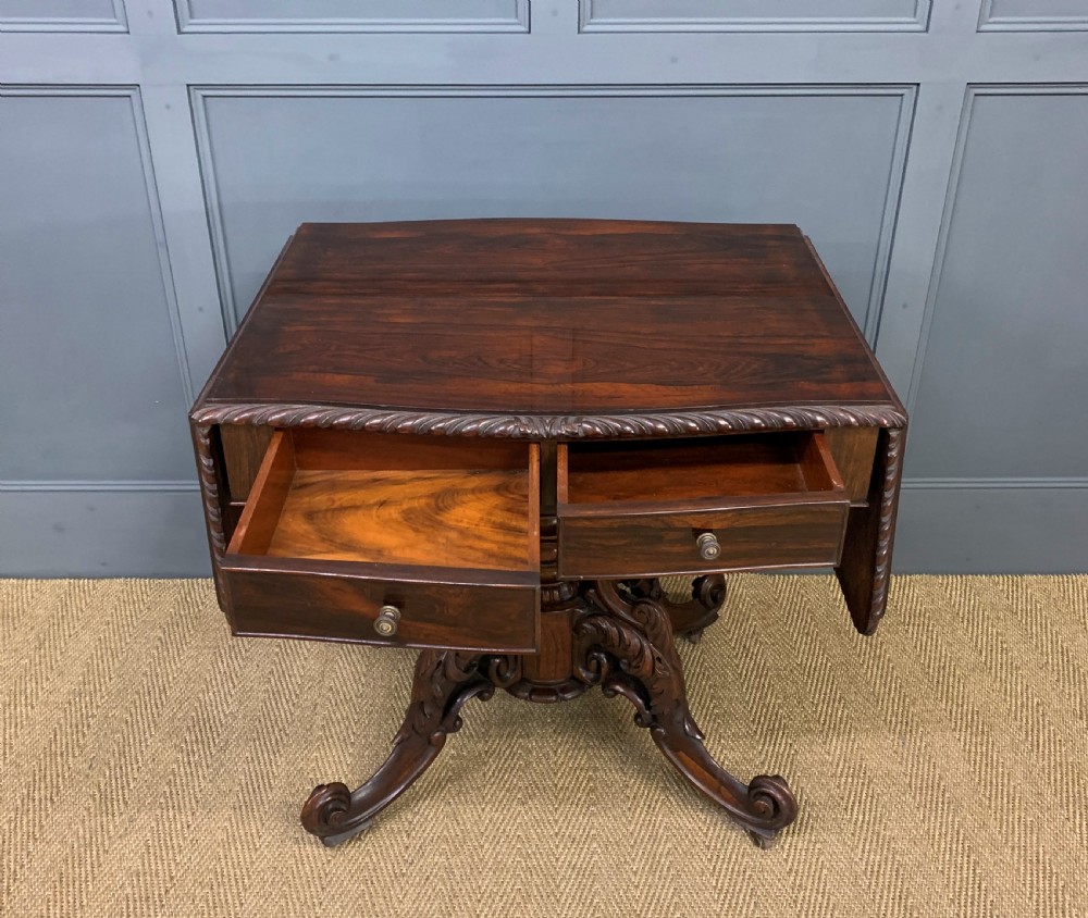 A 19th-century dark rosewood sofa table featuring drop leaves, two front frieze drawers, and an intricately carved central pedestal on scroll legs. View V