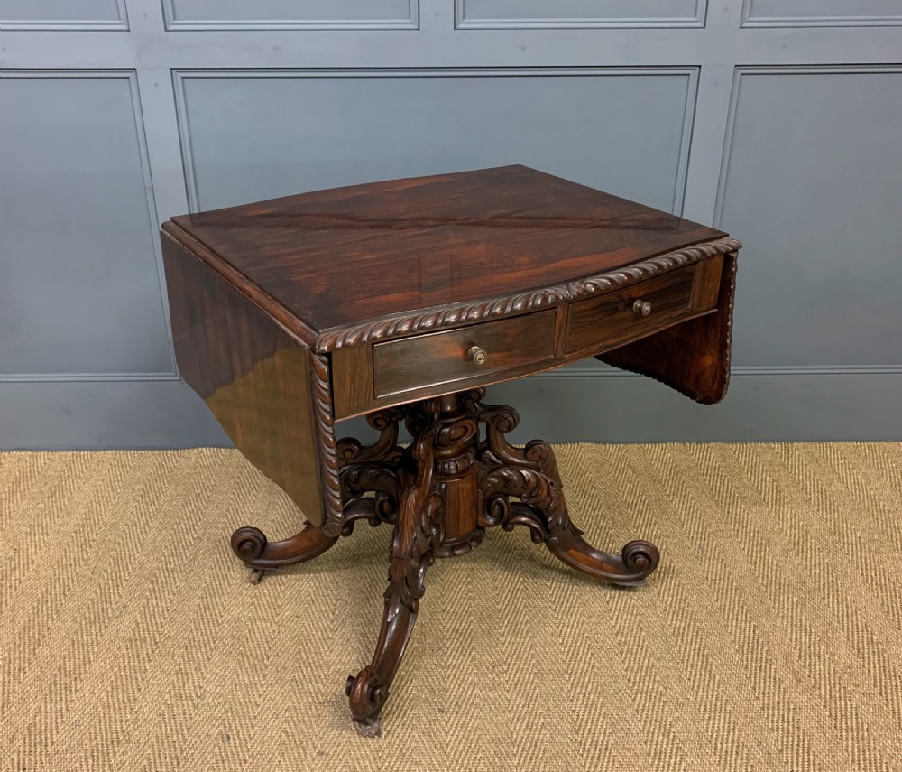 A 19th-century dark rosewood sofa table featuring drop leaves, two front frieze drawers, and an intricately carved central pedestal on scroll legs. View VII