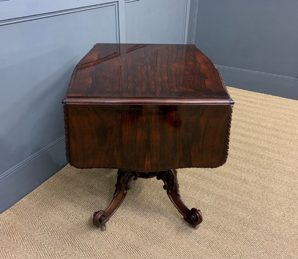 A 19th-century dark rosewood sofa table featuring drop leaves, two front frieze drawers, and an intricately carved central pedestal on scroll legs. View X