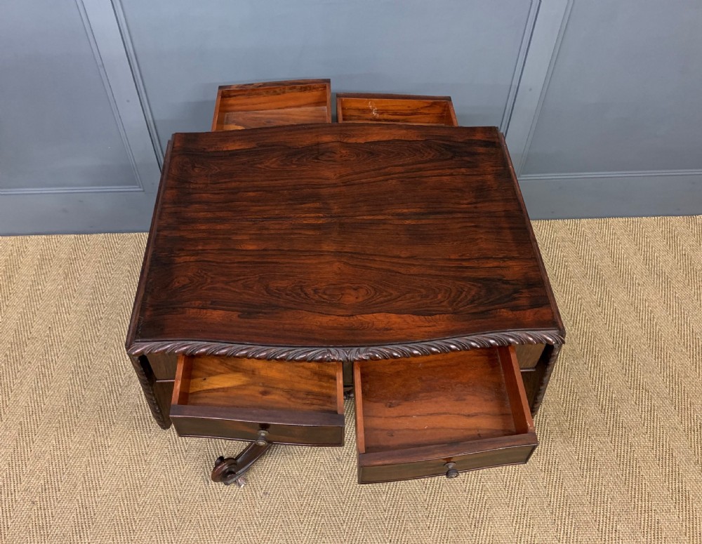 A 19th-century dark rosewood sofa table featuring drop leaves, two front frieze drawers, and an intricately carved central pedestal on scroll legs. View XII