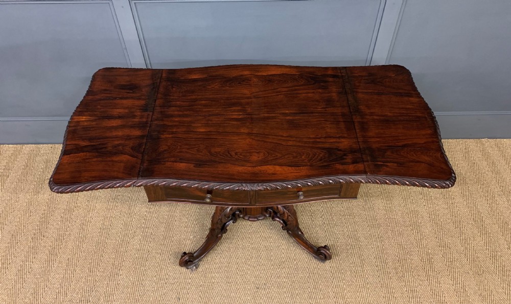 A 19th-century dark rosewood sofa table featuring drop leaves, two front frieze drawers, and an intricately carved central pedestal on scroll legs. View XV