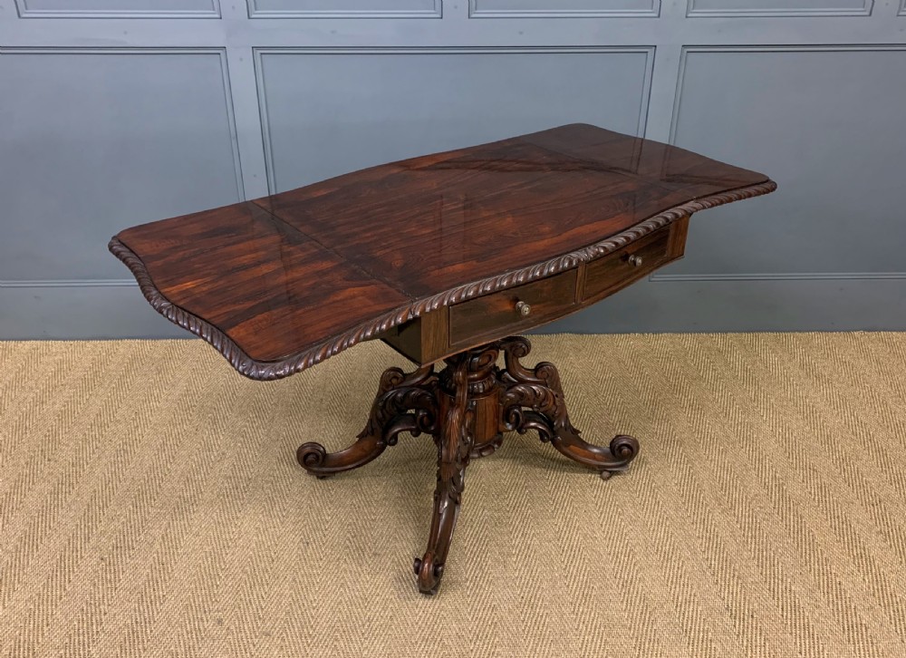 A 19th-century dark rosewood sofa table featuring drop leaves, two front frieze drawers, and an intricately carved central pedestal on scroll legs. View XX