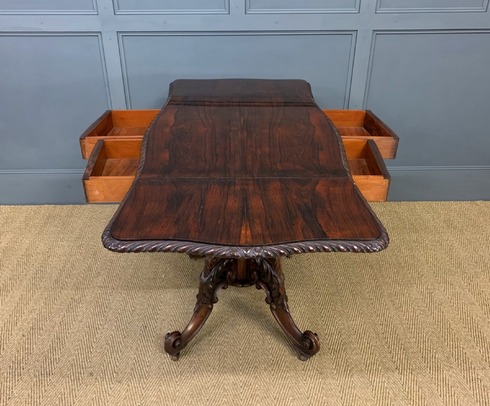 A 19th-century dark rosewood sofa table featuring drop leaves, two front frieze drawers, and an intricately carved central pedestal on scroll legs. View XXI