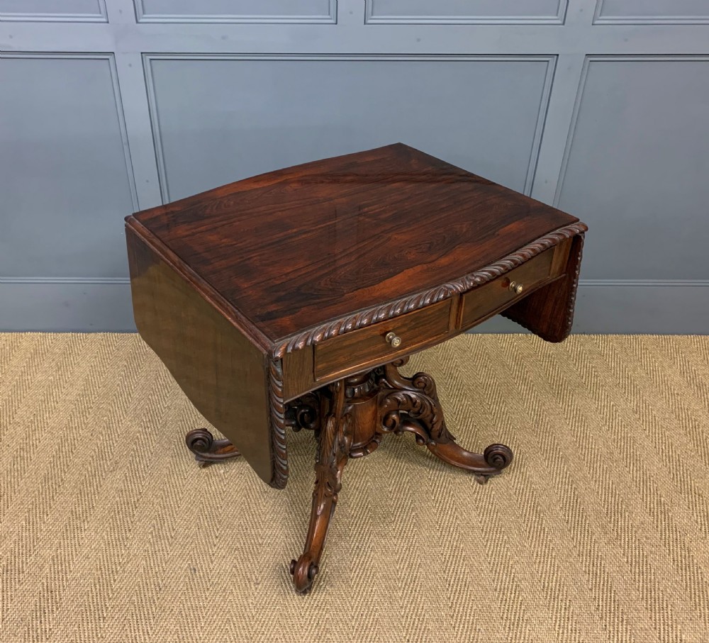 A 19th-century dark rosewood sofa table featuring drop leaves, two front frieze drawers, and an intricately carved central pedestal on scroll legs. View XXV