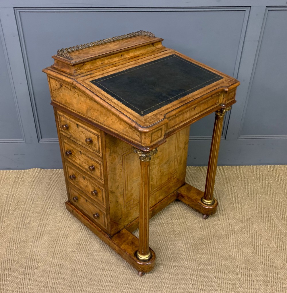 A Victorian burr walnut davenport desk featuring a sloped dark leather inset writing surface, brass gallery rail, side drawers, and fluted column supports.
