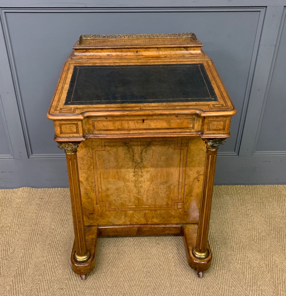 A Victorian burr walnut davenport desk featuring a sloped dark leather inset writing surface, brass gallery rail, side drawers, and fluted column supports. View II