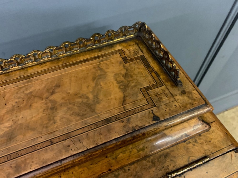 A Victorian burr walnut davenport desk featuring a sloped dark leather inset writing surface, brass gallery rail, side drawers, and fluted column supports. View V