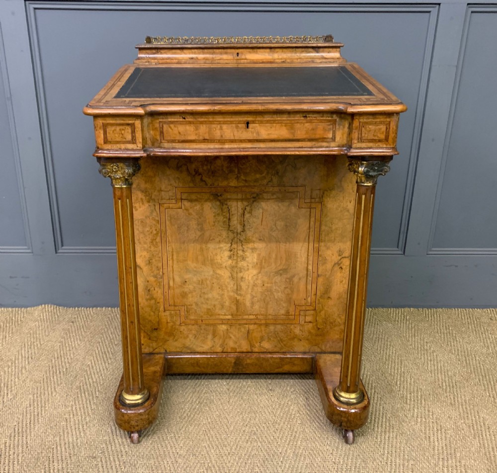 A Victorian burr walnut davenport desk featuring a sloped dark leather inset writing surface, brass gallery rail, side drawers, and fluted column supports. View VI