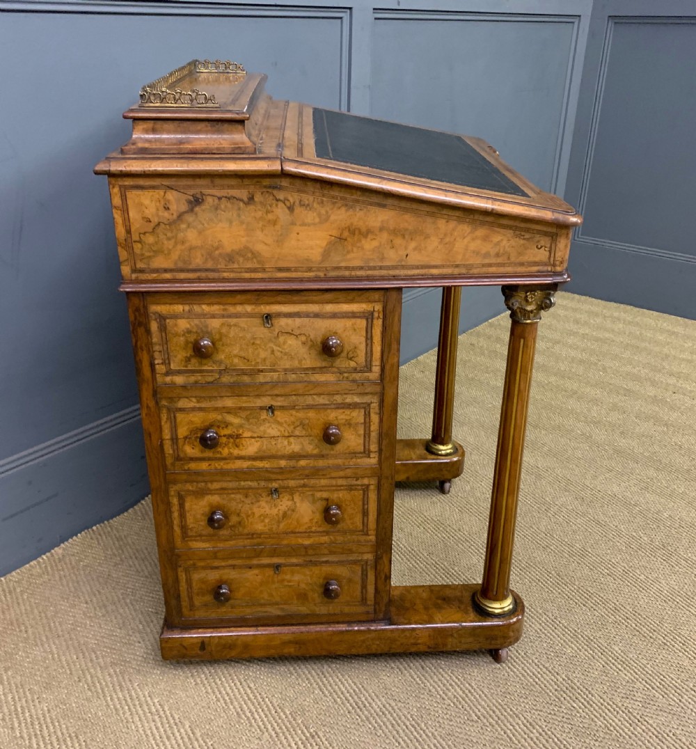 A Victorian burr walnut davenport desk featuring a sloped dark leather inset writing surface, brass gallery rail, side drawers, and fluted column supports. View XVI